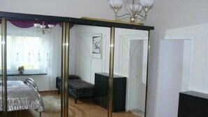 Une chambre avec une grande porte coulissante, un lit recouvert d’une couverture blanche, une commode et un lustre.