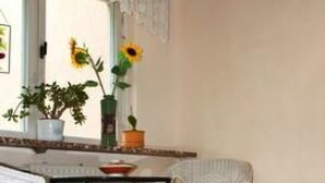 Un coin repas comprenant une table et deux chaises, un sol à motifs et une fenêtre donnant sur des tournesols.