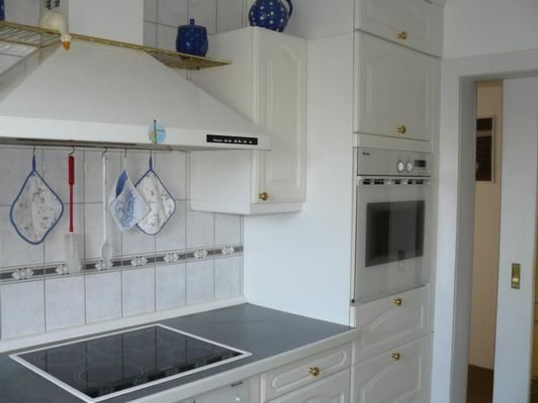 A kitchen with a built-in oven, a stovetop, and white cabinetry with gold handles.