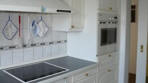 Une cuisine équipée d’un four encastré, d’une plaque de cuisson et de meubles blancs dotés de poignées dorées.