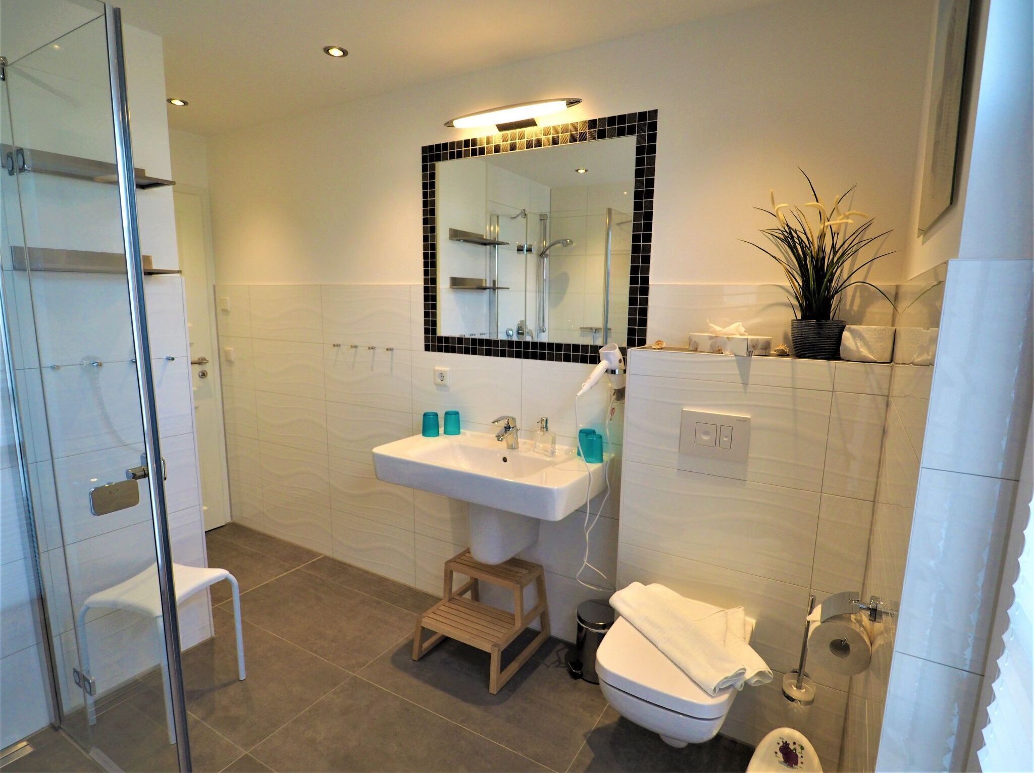Een moderne badkamer met een glazen douchecabine, een wit wastafelmeubel met een spiegel erboven en een toilet met een handdoek erop.