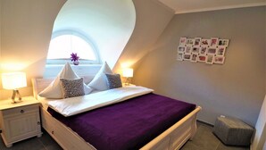 Un dormitorio con cama, mesitas de noche, ventana y una pared decorada con cuadros.