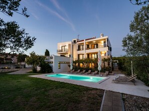 Ein modernes, zweigeschossiges Haus mit Swimmingpool, Sitzgelegenheiten im Freien und einem gepflegten Garten.
