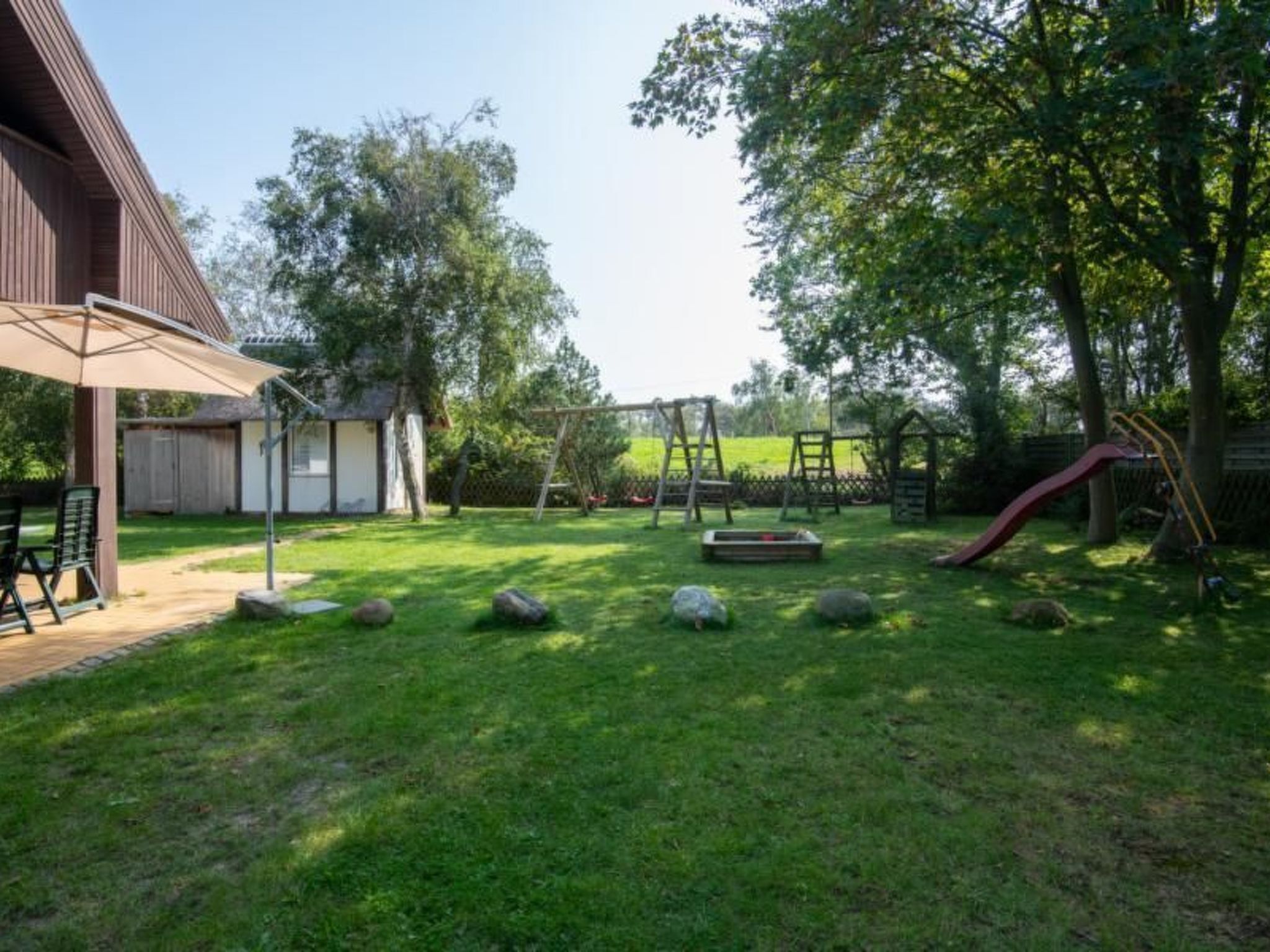 A backyard with a wooden deck, a swing set, and a slide.