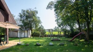 Een achtertuin met een houten terras, een schommel en een glijbaan.