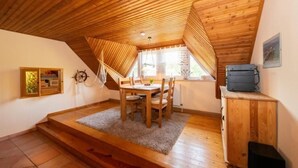 Een gezellig slaapkamer op zolder met houten balkenplafond, een eettafel en een klein kastje.