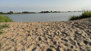 Une plage de sable fin, un lac paisible et des arbres qui se dessinent à l’horizon.