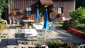 Ein Holzhaus mit Ziegeldach, Außenbereich mit Tischen und Stühlen sowie ein Garten mit Blumen.