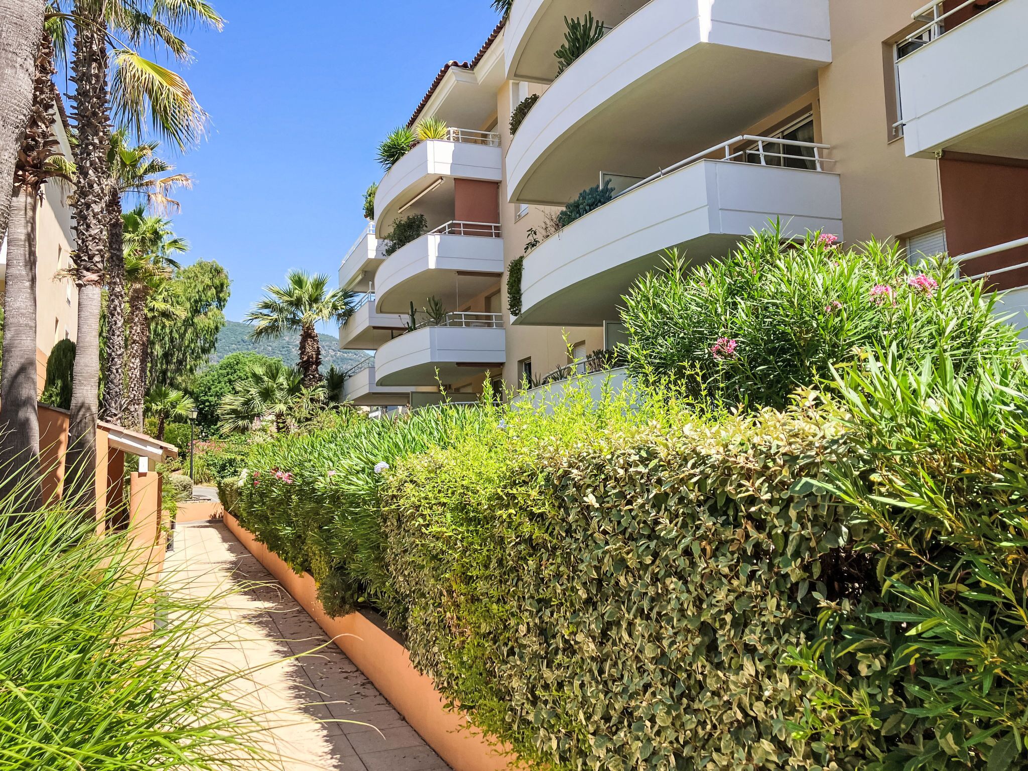 A multi-story residential building with balconies, a pathway, and lush greenery.