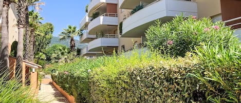 A multi-story residential building with balconies, a pathway, and lush greenery.