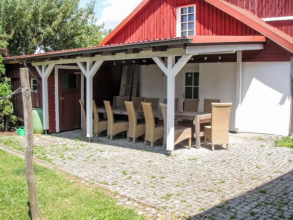 Un bâtiment rouge doté d’un patio couvert, d’un espace extérieur aménagé avec des sièges et d’une table en bois.