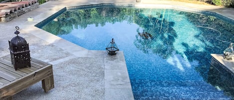 A swimming pool with a tiled edge, surrounded by a landscaped garden with various plants and a statue.