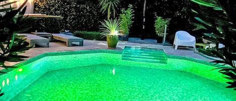 Una piscina con borde de azulejos, rodeada de mobiliario de exterior y plantas.