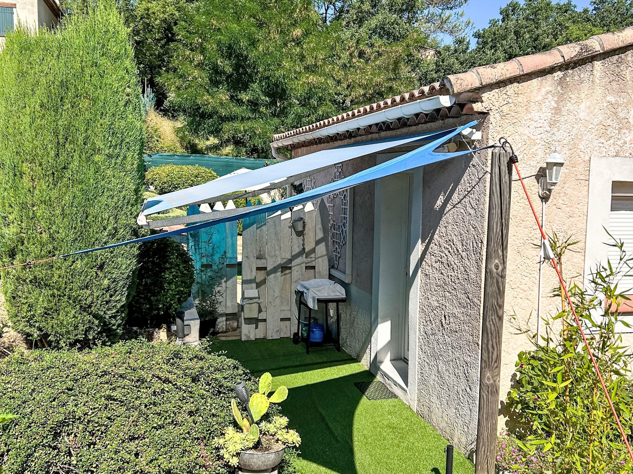 Une cour avec un petit jardin, un auvent bleu et un mur en pierre.
