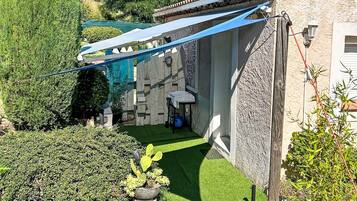 Une cour avec un petit jardin, un auvent bleu et un mur en pierre.