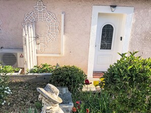 Un edifici amb una porta blanca, una decoració mural i un jardí ple de plantes i flors.