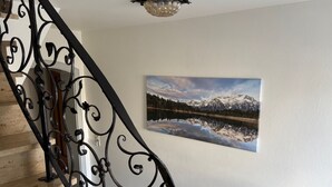 Un escalier orné de rampes en métal noir, un tableau représentant un paysage de montagne accroché au mur et un luminaire fixé au plafond.