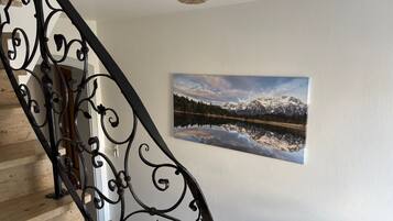 Eine Treppe mit aufwendiger schwarzer Metallgeländer, einem Wandbild von einer Berglandschaft und einer Deckenleuchte.