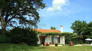 Ein Haus mit rotem Ziegeldach, Schornstein und einem Garten mit Rasen und Bäumen.