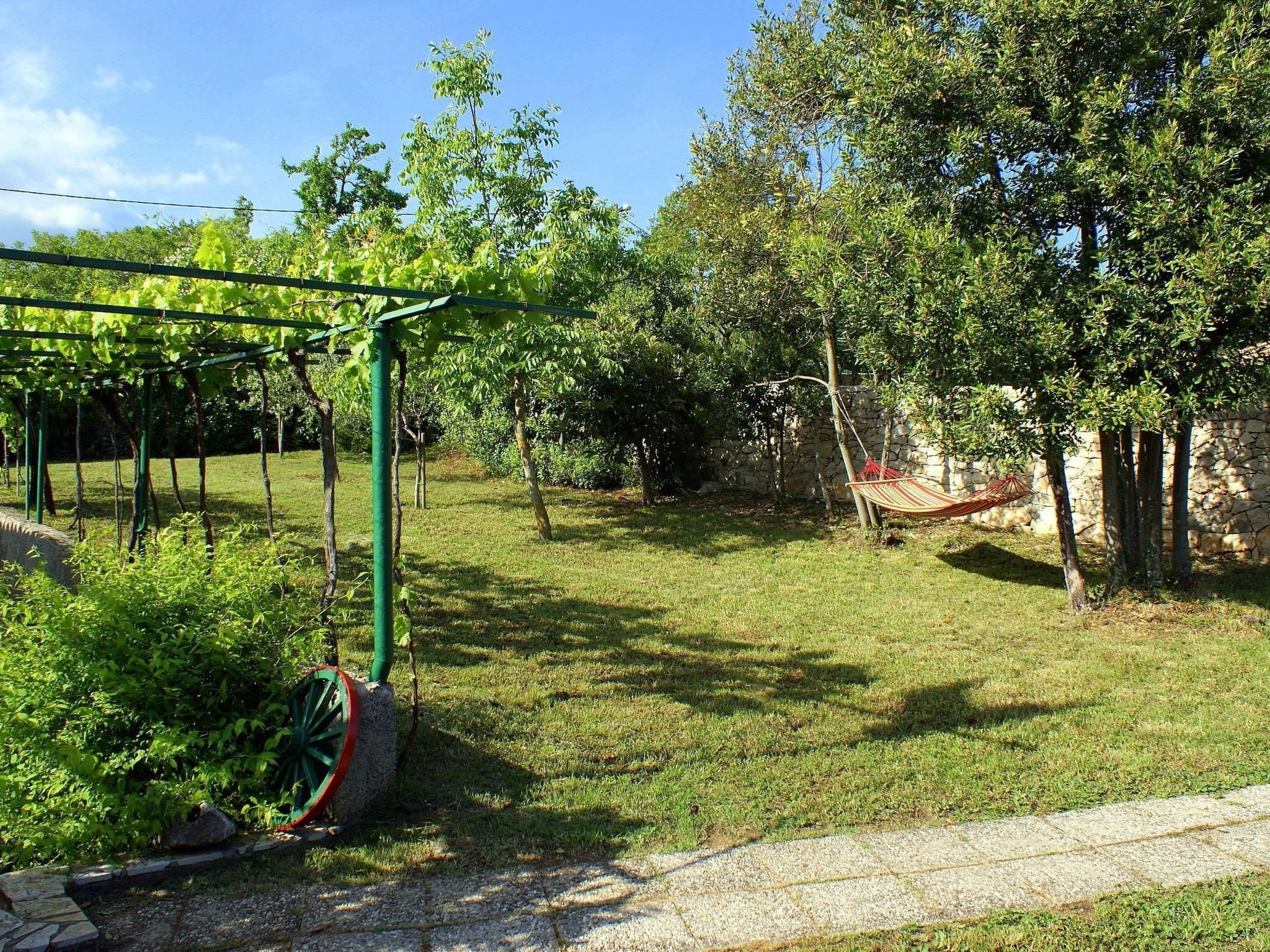 A garden with a hammock, a pergola, and a stone wall.