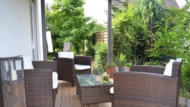 Un patio al aire libre con mobiliario de mimbre, una mesa de vidrio y plantas en macetas.