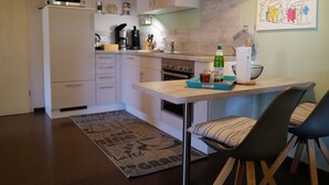 Una cocina moderna con armarios blancos, un microondas de acero inoxidable, una estufa a gas y una cafetera. En la encimera, hay una bandeja azul con condimentos y una botella de cerveza Da'iner.
