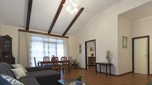 A spacious living room with a high ceiling, a dining area with wooden furniture, and a view of a cityscape through large windows. - mit Pool by Interhome (Medulin/Ližnjan)