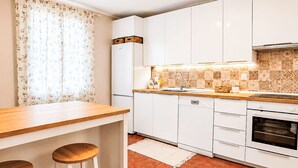 A kitchen with white cabinets, a wooden countertop, a built-in oven, and a window with floral curtains. - mit Pool by Interhome (Medulin/Ližnjan)