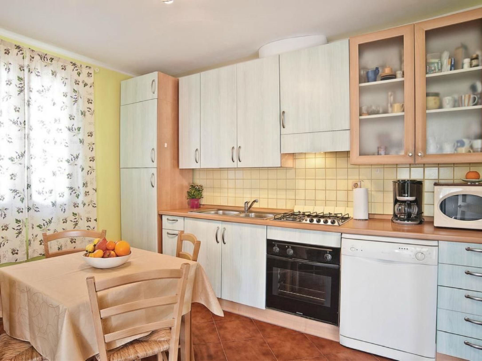 Une cuisine compacte avec des meubles blancs, une cuisinière à gaz, un four, un four à micro-ondes et un lave-vaisselle.