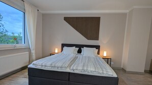 A modern bedroom with a large bed, two bedside lamps, and a view of trees through a window. - Haus Starkenburg by Interhome (Irmenach)