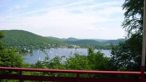 Vista su un lago da un balcone con ringhiera rossa, immerso nel verde e nelle colline.