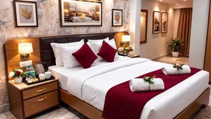 Une chambre d’hôtel avec un grand lit, une tête de lit en bois, des tables de chevet avec des lampes, des œuvres d’art encadrées accrochées aux murs et une plante en pot dans un coin.