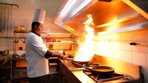 Un chef cuisinant avec une grande flamme dans une cuisine professionnelle.