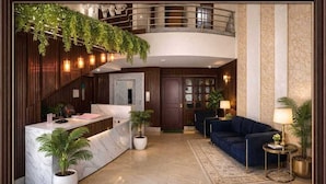 Un hall d’hôtel comprenant un comptoir d’accueil, un canapé bleu, des plantes en pot, un escalier et un lustre.