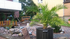 Ein Garten mit einer Palme, Felsen, einer hölzernen Bank und einer Statue.
