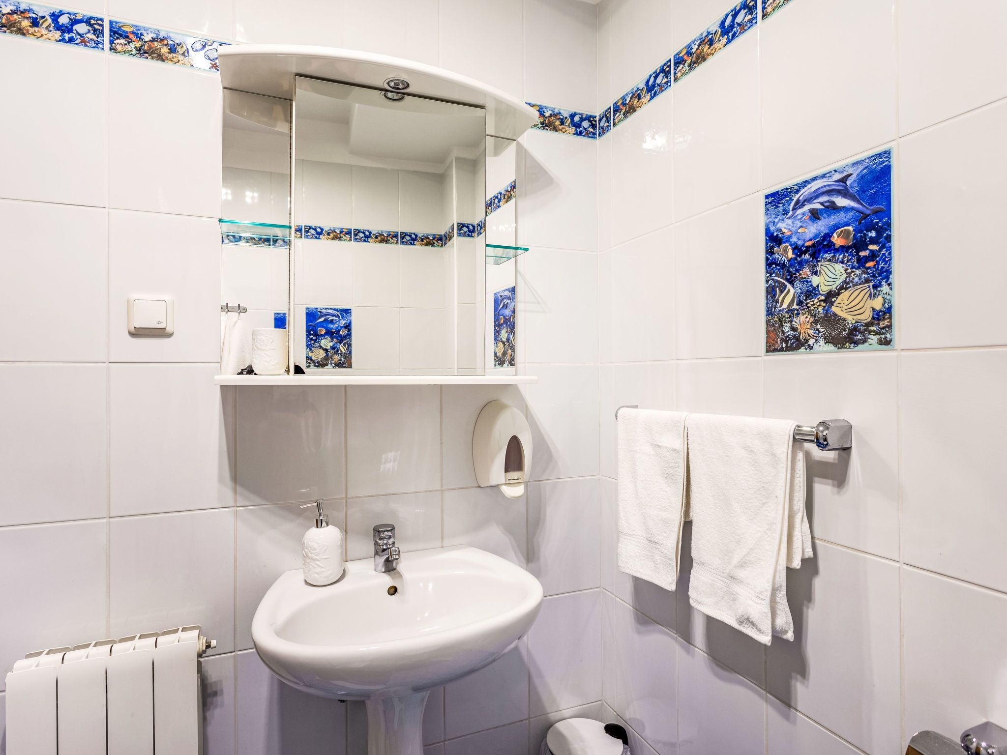 A bathroom with a white sink, a mirror, a towel rack, and decorative tiles.