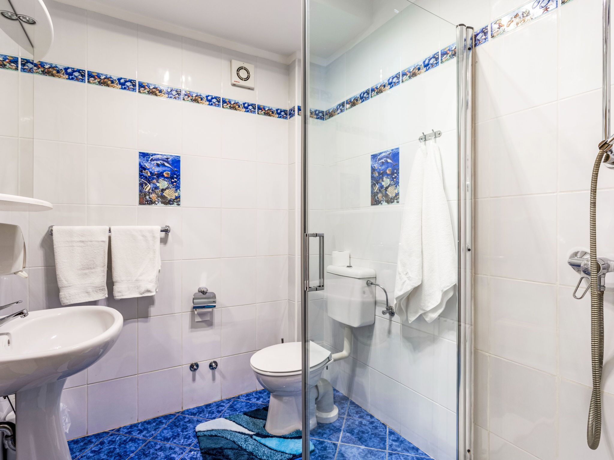 Un baño con mampara de vidrio, inodoro, lavabo y azulejos decorativos.
