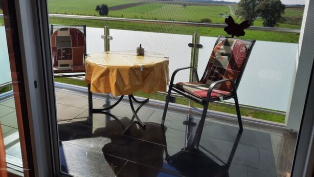 En balkon med et bord og stole, der udover et grønt landskab.