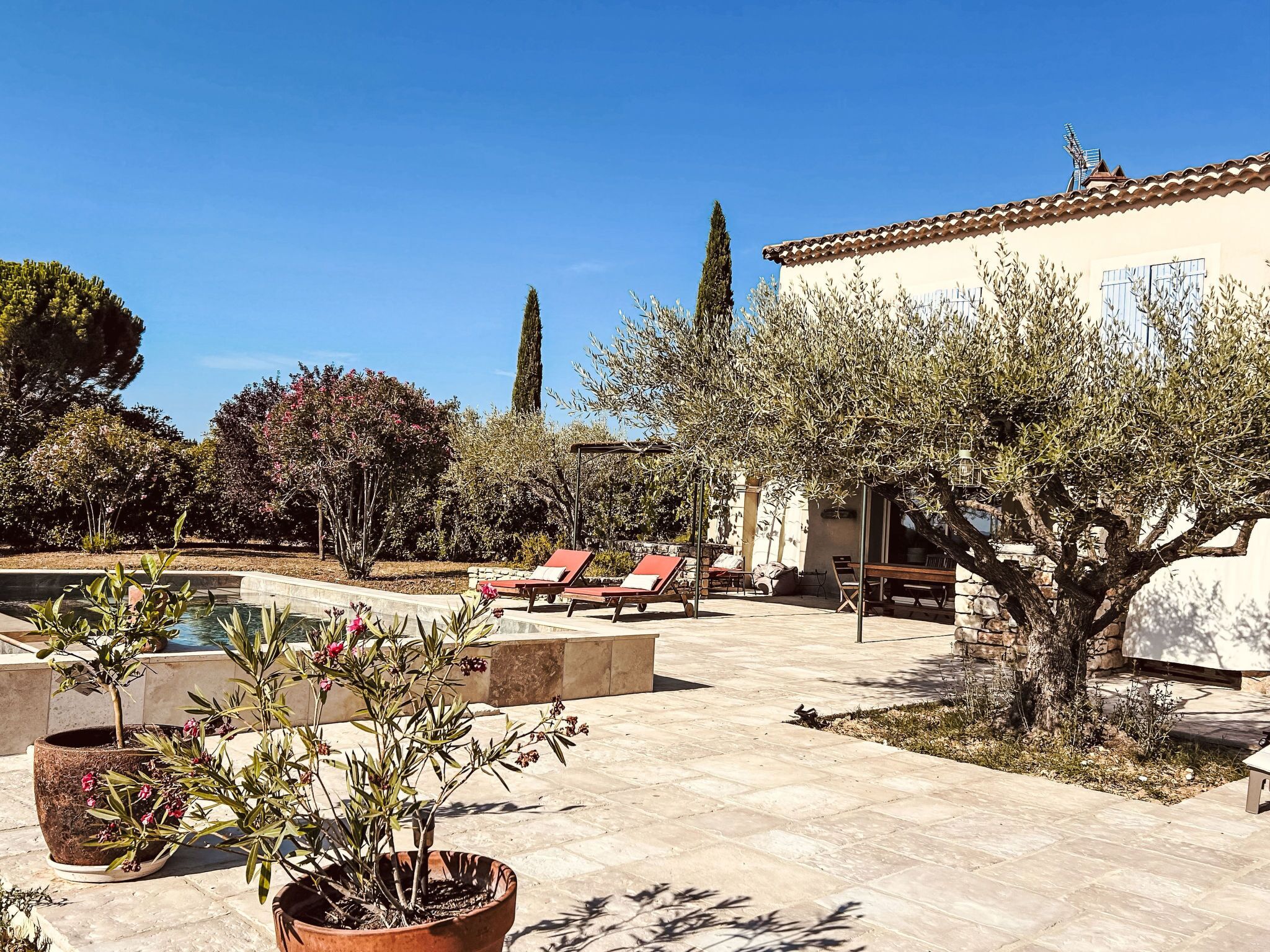 A pool area with lounge chairs, a stone patio, and a building with a tiled roof.