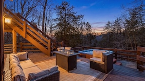 A wooden deck with outdoor furniture, a hot tub, and a staircase leading to an upper level.
