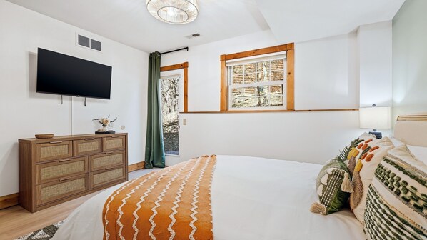 Ein Schlafzimmer mit Bett, Fernseher, Fenster mit Blick, einer Holzkommode und einer Lampe.
