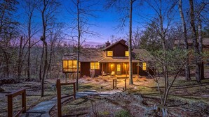 A two-story wooden house with a porch, surrounded by trees.