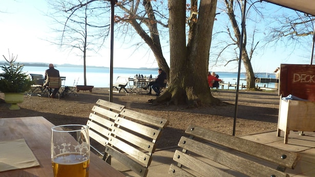 Een houten bankje en een glas bier bij een tafel aan het meer.