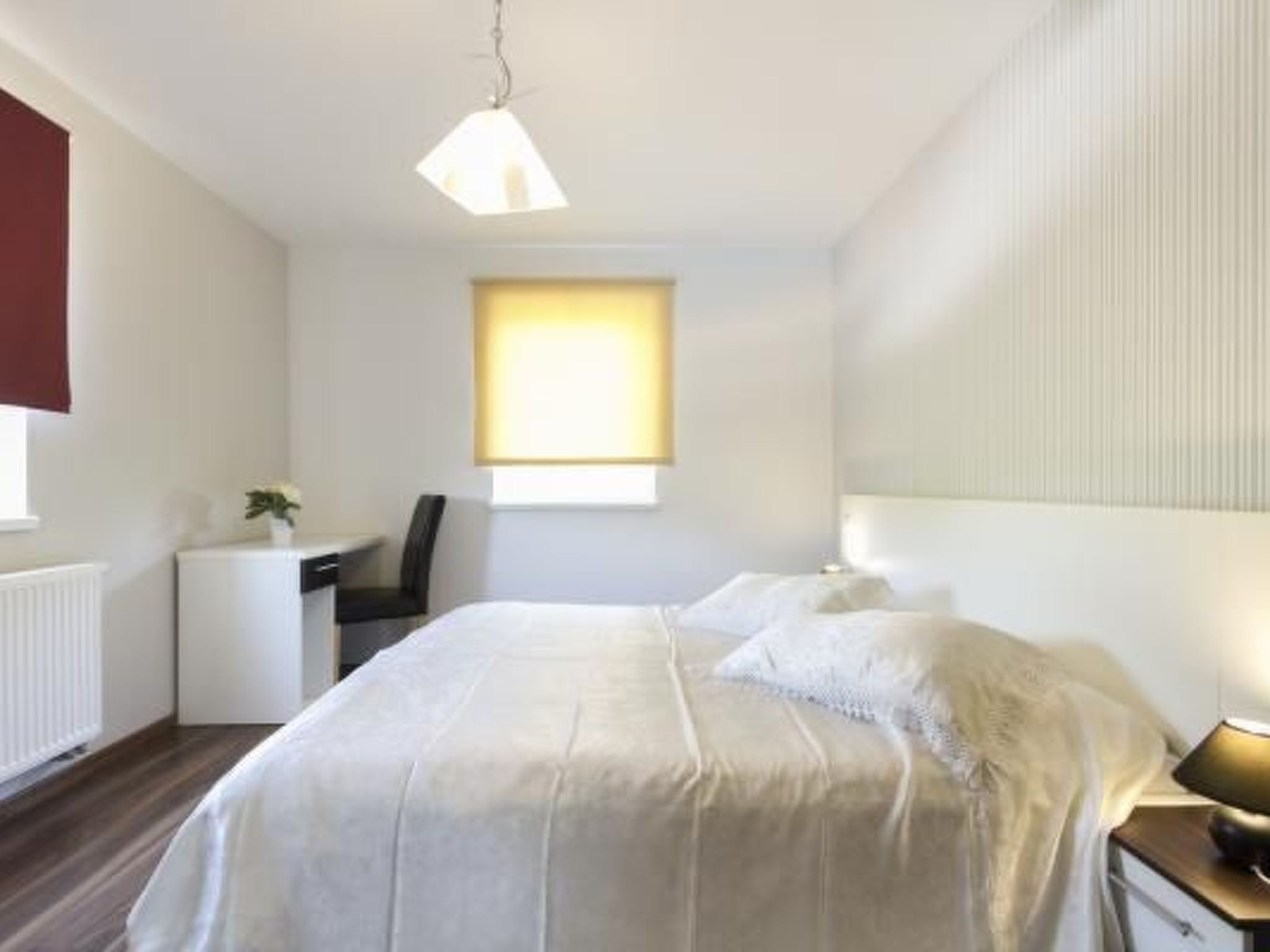 Ein Schlafzimmer mit Bett, Nachttisch, Lampe und einem Fenster mit Jalousien.