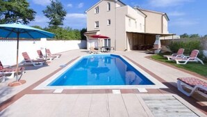 Piscina rectangular con sillones de descanso y zona de barbacoa en un patio trasero.