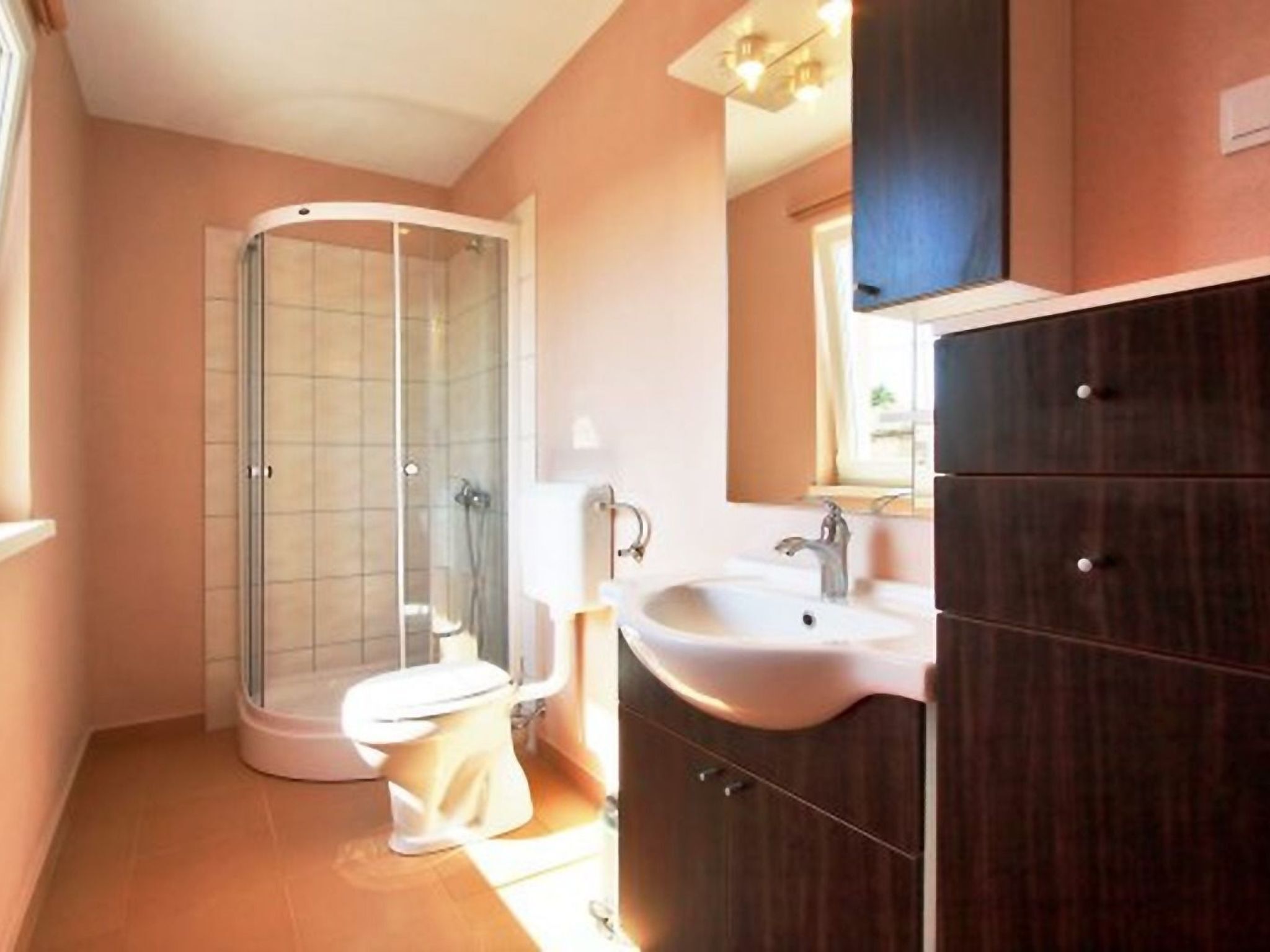 A bathroom with a glass shower enclosure, a toilet, a sink, and a dark wooden cabinet.