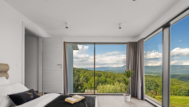Un dormitorio moderno con una cama grande, vistas a un bosque y una puerta corrediza al exterior.