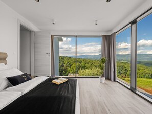 Camera moderna con un letto grande, vista su una foresta e una porta scorrevole che dà sull'esterno.