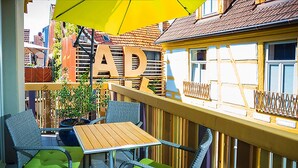 Un espacio al aire libre con mesas y sillas, un paraguas amarillo y un edificio con las letras "AD" a la vista.