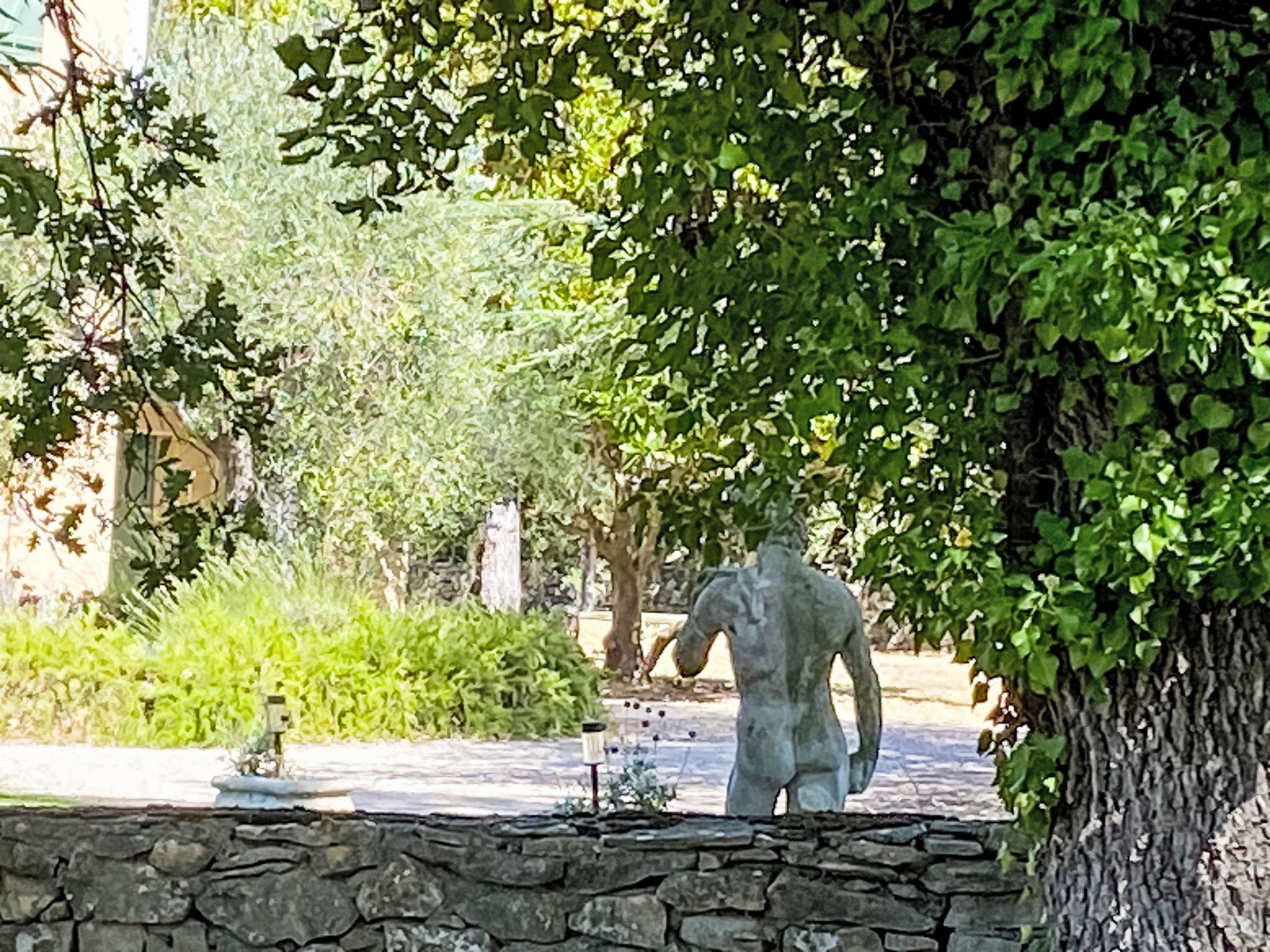 A stone wall, a statue, and lush greenery in a garden setting.
